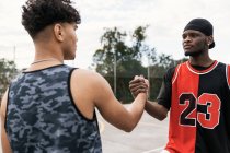 Seitenansicht afroamerikanischer männlicher Streetballspieler beim Händeschütteln, während sie auf einem Basketballplatz stehen und einander anschauen — Stockfoto