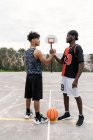 Side view of African American male streetball players shaking hands while standing on basketball playground and looking at each other — Stock Photo