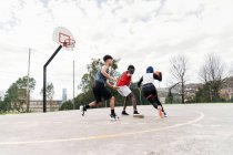 Multiethnic friends playing street basketball on sports ground in summer — Stock Photo