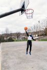 Muslim female streetball player jumping above ground and scoring ball in basketball hoop — Stock Photo