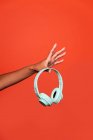 Crop femme afro-américaine anonyme montrant écouteurs sans fil sur la main tendue sur fond rouge en studio — Photo de stock