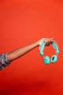 Crop femme afro-américaine anonyme montrant écouteurs sans fil sur la main tendue sur fond rouge en studio — Photo de stock