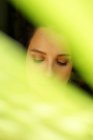 Young lonely gentle female with eyes closed standing behind colorful green plant leaf — Stock Photo