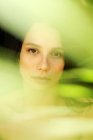 Giovane donna gentile solitario con gli occhi chiusi in piedi dietro colorato foglia di pianta verde — Foto stock