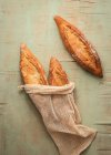 Top view composition of delicious crispy artisan sourtough bread loaves packed in burlap bags on green background — стоковое фото