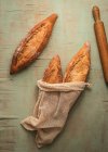 Top view composition of delicious crispy artisan sourtough bread loaves packed in burlap bags on green background — стоковое фото