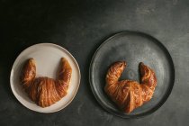 Top view composition with appetizing freshly baked crusty croissants served on white and black plates on table — Stock Photo