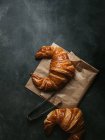 Top view composition with tasty fresh crusty croissants placed with paper bag and metal tongs on black background — Stock Photo