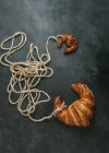 From above of delicious freshly baked traditional croissant wrapped with rope on black background — Stock Photo