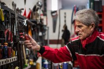Seitenansicht eines gealterten gelernten Reparateurs, der während seiner Arbeit in der Werkstatt professionelle Werkzeuge aus dem Regal holt — Stockfoto