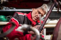 Senior männlicher Mechaniker repariert altes rostiges zerlegtes Motorrad während er in einer professionellen Werkstatt arbeitet — Stockfoto