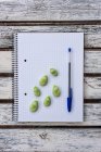 Von oben rohe grüne Bohnen und Stift auf Notizblock auf Holztisch gelegt — Stockfoto