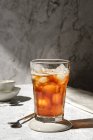 Glass of refreshing cold tea with ice cubes served on glass on table with spoon in sunlight — Stock Photo