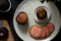 Vista superior de tomates pretos frescos inteiros e fatiados na mesa com abacate e hortelã verde durante a preparação da refeição saudável — Fotografia de Stock