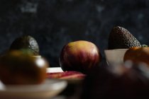 Frische ganze und in Scheiben geschnittene schwarze Tomaten auf dem Tisch mit Avocado bei der Zubereitung einer gesunden Mahlzeit — Stockfoto