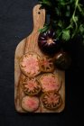 Draufsicht auf frische reife, in Scheiben geschnittene schwarze Tomaten und grüne Minzstiele auf einem Holzschneidebrett auf schwarzem Hintergrund — Stockfoto