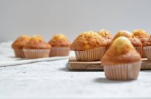 Délicieux muffins sucrés maison fraîchement cuits dans des tasses en papier disposées sur la table — Photo de stock