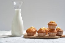 Смачні домашні свіжоспечені солодкі кекси в паперових стаканчиках, розташованих на столі зі скляною банкою свіжого молока — стокове фото
