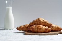Deliciosos croissants e garrafa de leite colocados na mesa para o café da manhã na cozinha — Fotografia de Stock