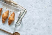 Vista superior de croissants frescos gostosos colocados na bandeja de metal na mesa na cozinha — Fotografia de Stock