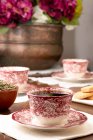 Copos de cerâmica ornamentais com café servido na mesa com flores para chá no quarto aconchegante em casa — Fotografia de Stock