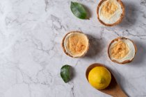 Vista dall'alto di deliziose crostate di meringa fatte in casa poste sul tavolo con limone fresco e foglie verdi — Foto stock
