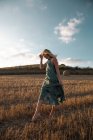 Peaceful female in elegant dress standing on dry field in rural area and looking down — Stock Photo