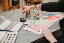 Ernte unkenntlich weibliche Künstlerin, die mit Aquarellen auf Papier malt, während sie am Tisch im Kunstatelier sitzt — Stockfoto