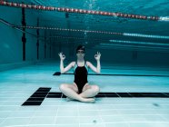 Frau sitzt in Yoga-Haltung unter Wasser und blickt in Kamera — Stockfoto