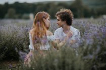 Спокойная пара, сидящая на лавандовом поле с цветущими цветами и смотрящая друг на друга — стоковое фото