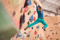 Visão traseira de baixo ângulo do atleta feminino anônimo escalando parede artificial durante o treino de pedregulho no ginásio profissional — Fotografia de Stock