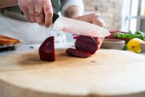 Cortar irreconhecível fêmea corte beterraba fresca com faca enquanto prepara o almoço vegetariano na cozinha da casa — Fotografia de Stock