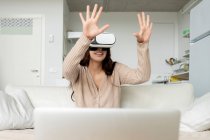Femme gaie méconnaissable avec manette de jeu expérimentant la réalité virtuelle dans les lunettes tout en jouant à un jeu vidéo sur le canapé dans la maison — Photo de stock
