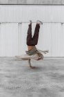 Bailarina masculina irreconocible mostrando movimiento breakdance mientras se equilibra en brazos y realiza Hand Hops en suelo de hormigón en zona urbana - foto de stock