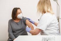 Ärztin in Schutzuniform und Latexhandschuhen impft ältere Patientin in Klinik während des Coronavirus-Ausbruchs — Stockfoto