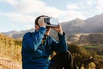 Цікавий чоловік мандрівник сидить на пагорбі і відчуває віртуальну реальність в окулярах в горах в сонячний день — стокове фото