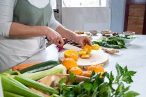 Врожай невизначений жіночий пілінг стиглих соковитих апельсинів з ножем на дерев'яній дошці за кухонним столом — стокове фото