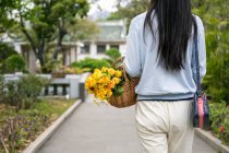 Detail der schönen Asiatin in einem Park, während sie einen Weidenkorb mit gelben Blumen trägt. — Stockfoto