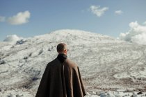Вид ззаду анонімного чоловічого туриста на мисі, який захоплюється засніженою горою під блакитним хмарним небом взимку — стокове фото