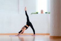 Side view of female in sportswear showing Three Legged Downward Facing Dog pose in room — Stock Photo