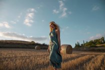 Peaceful female in elegant dress standing on dry field in rural area and looking away — Stock Photo