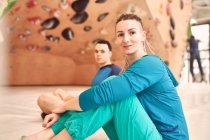 Seitenansicht weiblicher und männlicher Bergsteiger, die auf dem Boden in der Nähe einer künstlichen Wand in einem modernen Boulderzentrum sitzen und dabei in die Kamera schauen — Stockfoto