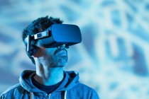 Unrecognizable bearded male in hoodie and modern headset exploring virtual reality in neon light — Stock Photo