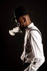Vista lateral de masculino afro-americano masculino em camisa branca e chapéu exalando vapor enquanto fuma e cigarro — Fotografia de Stock