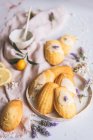 Вид сверху на вкусные мадлен на тарелке между свежими ломтиками лимона и цветущими веточками лаванды на мятой ткани — стоковое фото