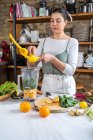 Contenido hembra exprimiendo jugo de limón en hojas de acelga en un tazón de licuadora mientras prepara una bebida saludable en la cocina de la casa - foto de stock
