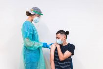 Female medical specialist in protective uniform, latex gloves and face mask vaccinating hispanic man patient in clinic during coronavirus outbreak — Stock Photo