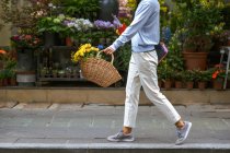 Vista laterale del corpo della ragazza che trasporta un cesto di fiori mentre cammina — Foto stock