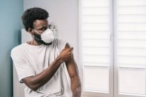 Paciente afroamericano que sostiene algodón con el brazo desinfectante de alcohol después del procedimiento de vacuna covid en la clínica durante el brote de coronavirus - foto de stock