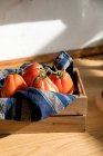 Високий кут свіжих стиглих червоних помідорів, розміщених на натуральному дерев'яному підносі з серветкою на домашній кухні — стокове фото